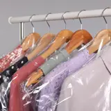 Dry-cleaning service. Many different clothes in plastic bags hanging on rack against grey background, closeup